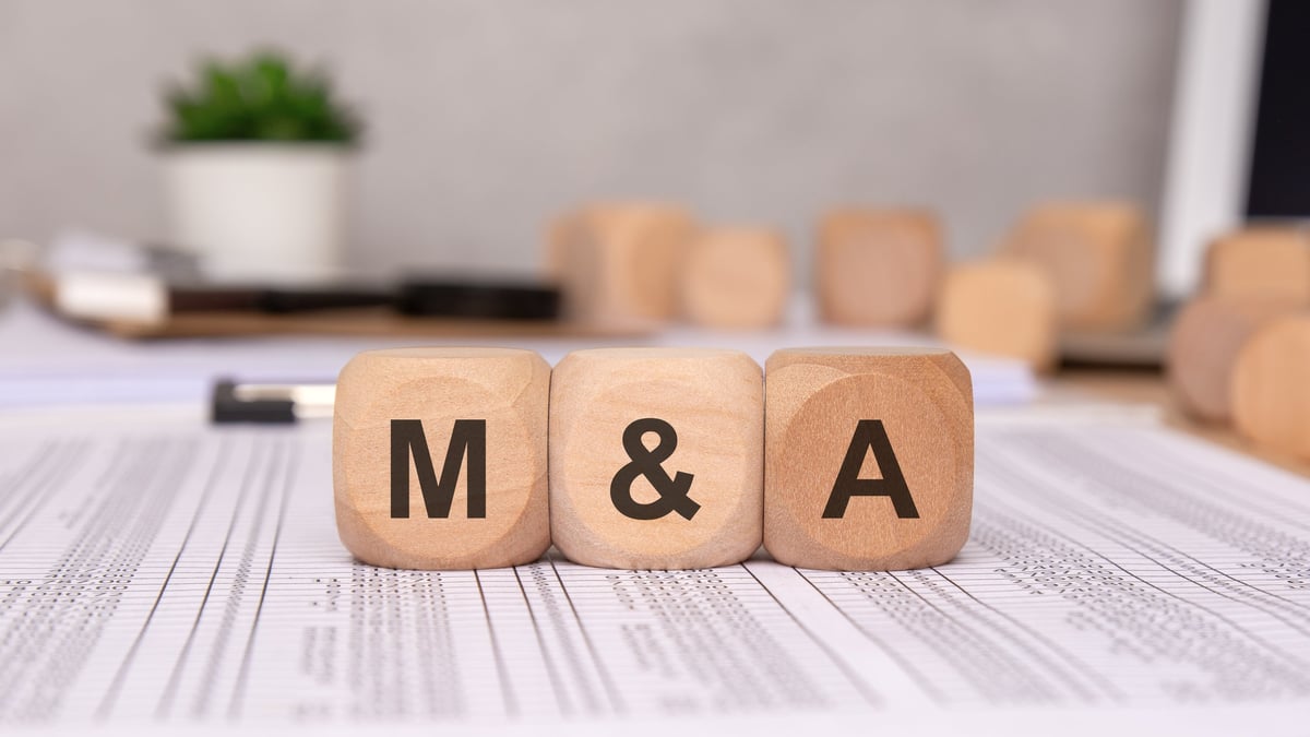 Three wooden cubes on financial spreadsheets, representing business mergers and acquisitions