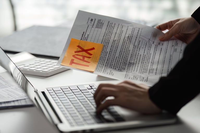 A person handles tax forms while using a laptop, highlighting the critical task of preparing for tax season.