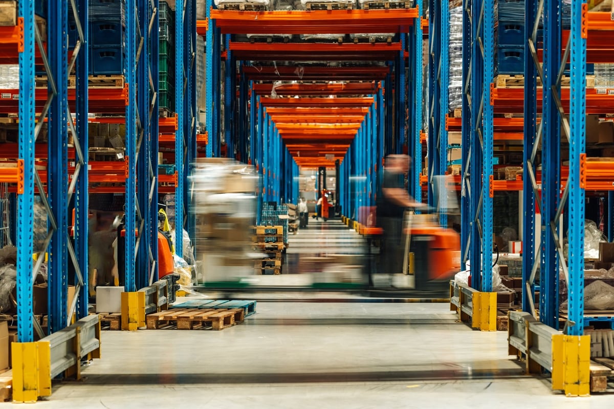 Warehouse distribution center with workers moving parcels and freight on shelving, illustrating rising shipping logistics costs