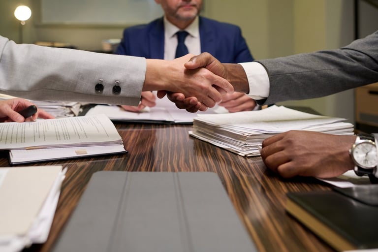 Caucasian woman and Black man shaking hands over stack of documents during business meeting