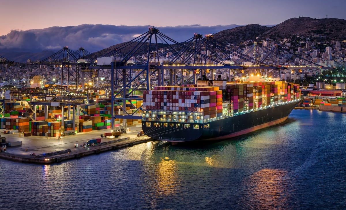 Container super cargo ship being unloaded and loaded by cranes and trucks in a commercial terminal during evening