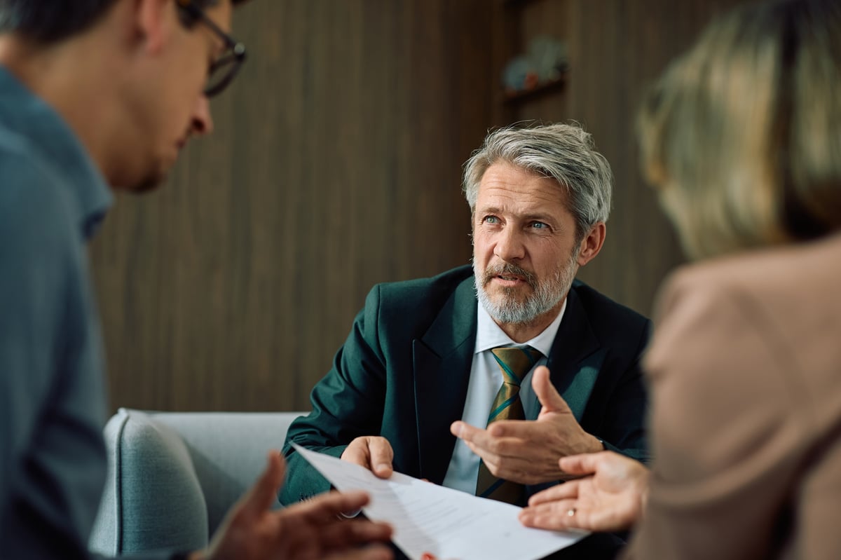 Mature financial advisor talking to a couple while going through paperwork during the meeting.