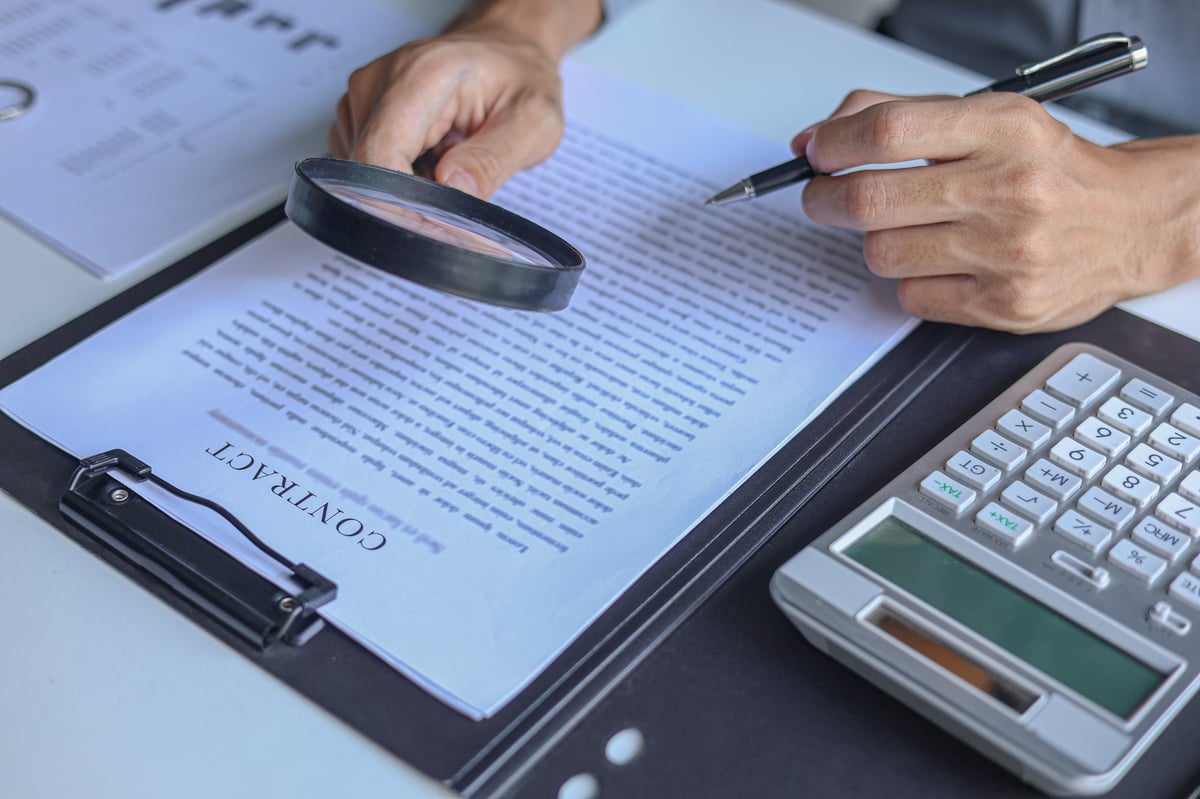 Business professional carefully reviewing a vendor contract and agreement using a magnifying glass